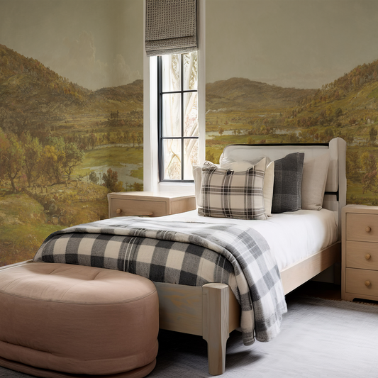 Bedroom with checkered blanket, pillows, and a beige ottoman in front of landscape wall art.
