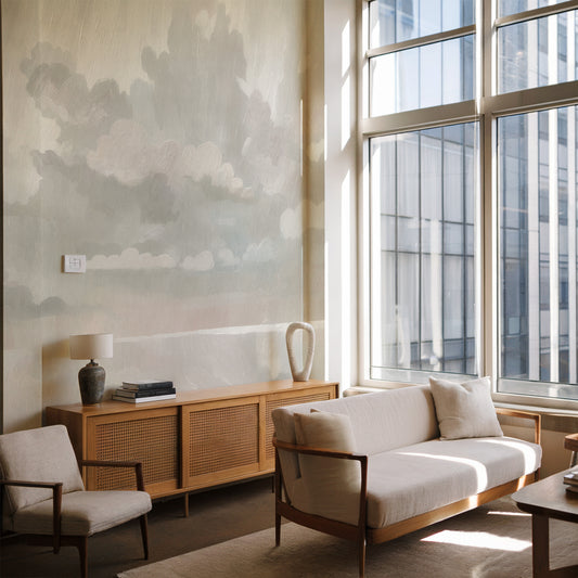 Modern living room with a sofa, armchair, and wooden cabinet near large windows.