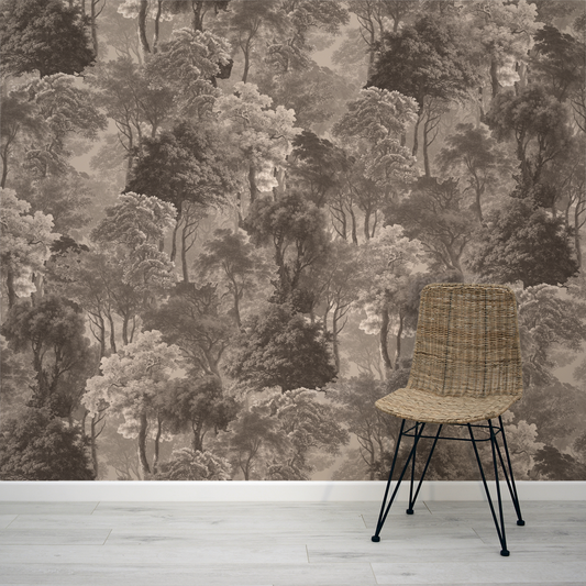 Wicker chair in front of a forest wallpaper design on a wall.