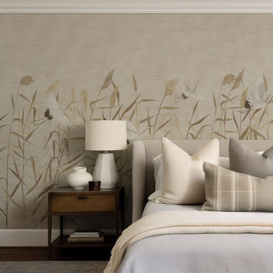 A styled bedroom scene featuring a bed with neutral-toned bedding and pillows, a wooden nightstand with a white lamp and ceramic vase, and a wall covered in a beige botanical wallpaper with tan and white floral and grass motifs.