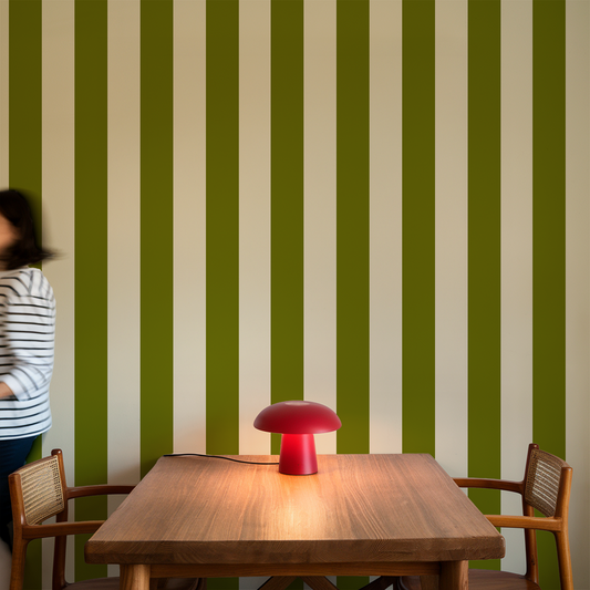Wooden table with a red lamp against a green and white striped wall.