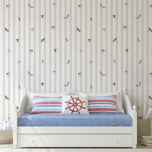 White crib with striped bedding and decorative pillows against a striped wallpaper wall.