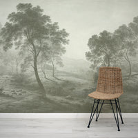 Wicker chair in front of a wall mural depicting a misty green landscape with trees.