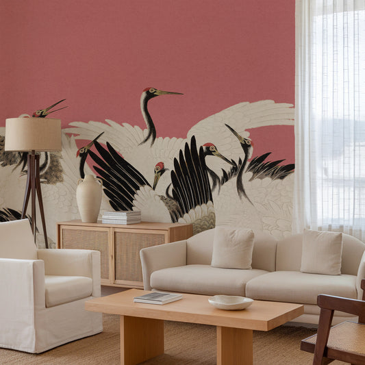 A styled living room featuring a large wall mural with black and white cranes on a dusty pink background, styled with a cream sofa, wooden coffee table, and a floor lamp.