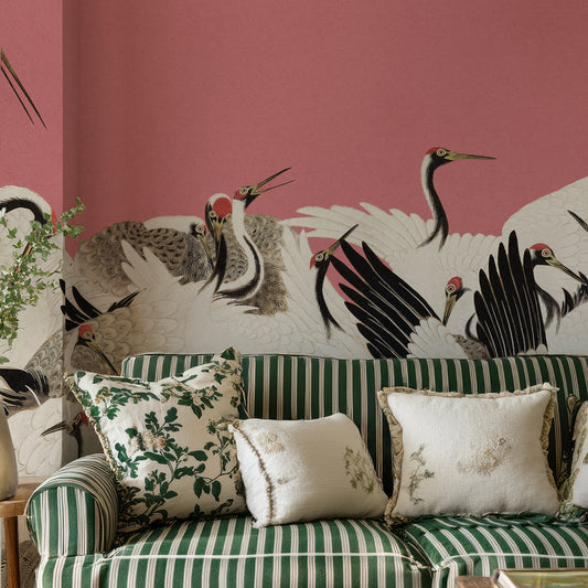 A styled interior scene with a green-and-white striped sofa, decorative throw pillows, and a large wall mural of cranes on a dusty pink background.