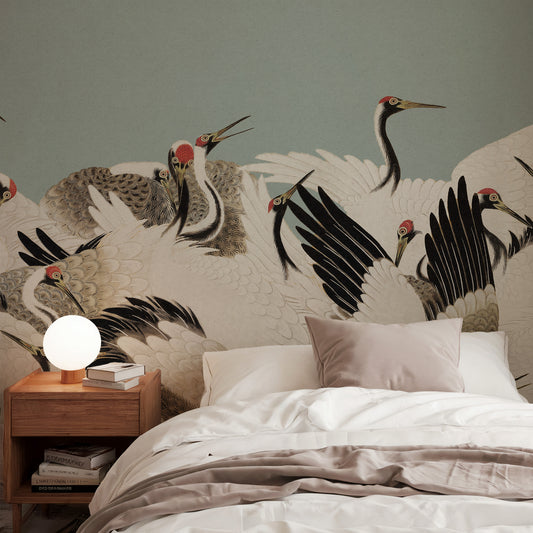 A styled bedroom scene featuring a large wall mural of cranes in flight behind a neatly made bed with white linens and a wooden bedside table with a glowing spherical lamp.