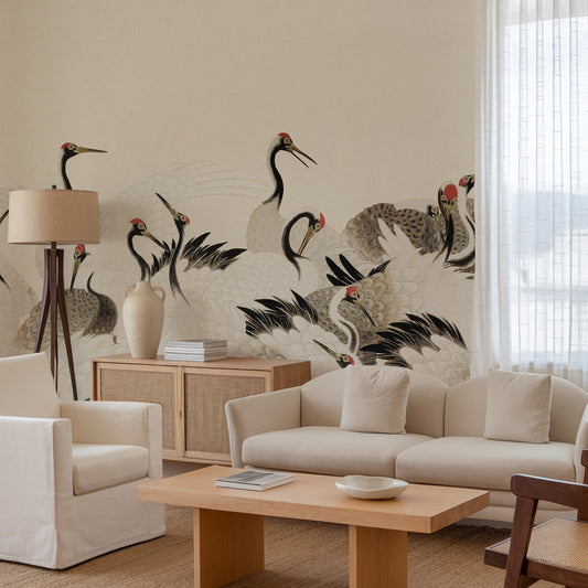 A styled living room featuring a large wall mural with black and white cranes and red accents on a beige background. The room is furnished with a cream-colored sofa, armchair, wooden coffee table, and a floor lamp.