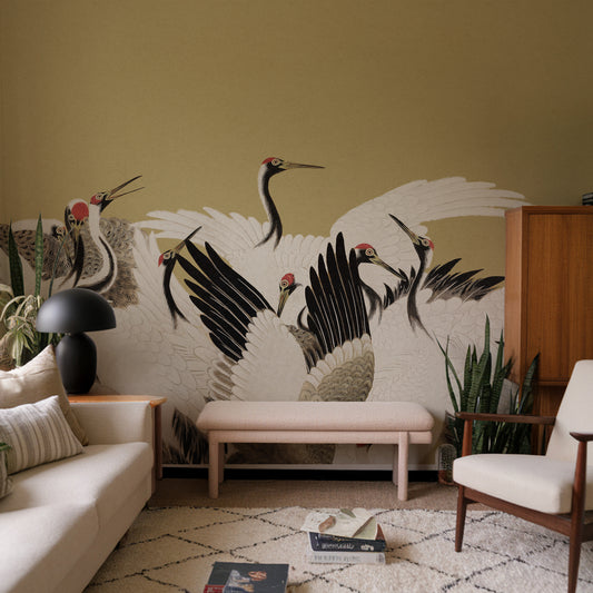 A large wall mural featuring black and white cranes with red heads, displayed in a styled living room setting with a beige sofa, wooden chair, and bench.