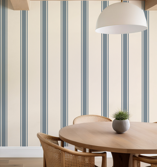 Dining area with a round wooden table and chairs against a wall with blue vertical stripes.