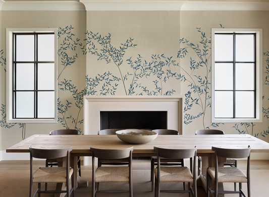 Dining room with a long table and chairs against a wall with floral wallpaper.
