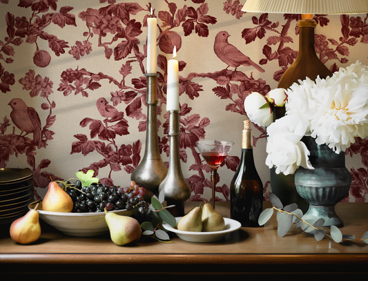 Dining table with fruit, candles, and a vase against floral wallpaper